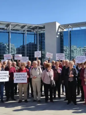 Grupo de jubilados españoles debatiendo sobre la reforma de pensiones frente a un edificio gubernamental moderno.