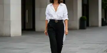 Mulher com look minimalista Shein, camisa branca oversized, calça preta de alfaiataria e joias douradas simples, caminhando em cenário urbano moderno.