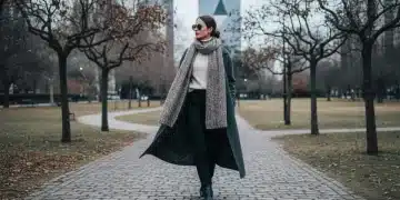 Mulher estilosa com casaco de lã, suéter de gola alta e botas, caminhando em um parque urbano durante o inverno de 2026 no Brasil.