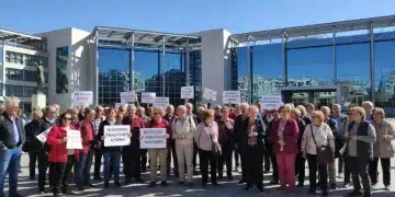 Grupo de jubilados españoles debatiendo sobre la reforma de pensiones frente a un edificio gubernamental moderno.